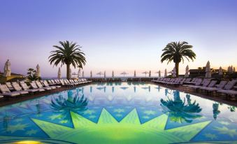 a large , oval - shaped pool with palm trees and lounge chairs is the centerpiece of a tropical resort at Montage Laguna Beach