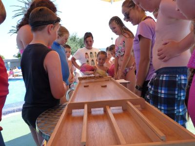 a group of children and adults are gathered around a long wooden table , playing a board game at Club Mac Club Mac - All Inclusive Family Resort Photo