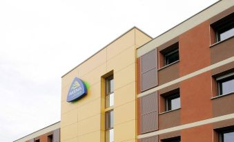 a modern hotel building with multiple floors , large windows , and a logo on the front at Sure Hotel by Best Western St-Amand-Les-Eaux