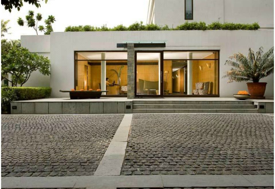 a modern building with large glass windows and a gray stone driveway leading to the entrance at The Manor - New Delhi