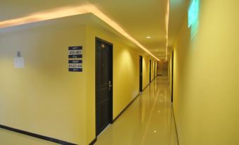 a long , well - lit hallway with yellow walls and black doors , including one with a sign on it at White Inn Nongkhai Hotel