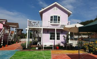 a pink house with a balcony and white railing is surrounded by colorful pavers and has a soccer field in front at Bunny Hill Resort