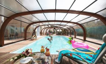 a large swimming pool with a glass roof , surrounded by a wooden deck and lounge chairs at Mercure Castres l'Occitan