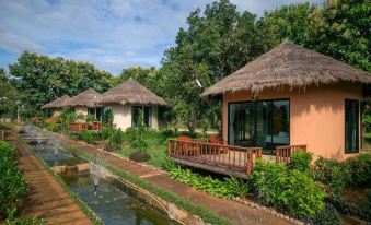 a group of small houses with thatched roofs situated next to each other on a grassy field , surrounded by trees at Aurora Resort Chiangdao