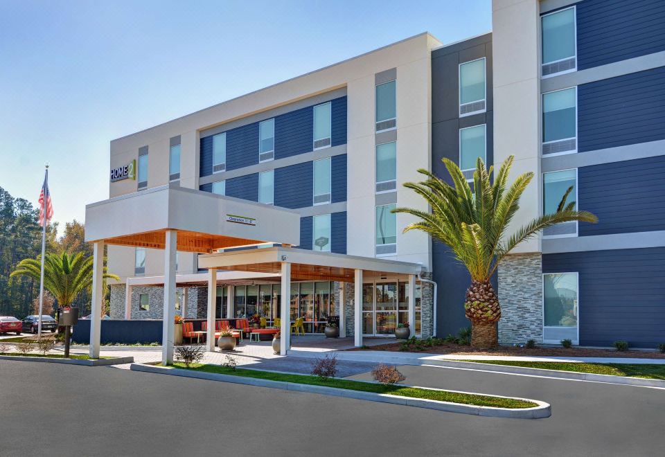 a modern hotel building with a large sign on the front , surrounded by palm trees and other greenery at Home2 Suites by Hilton Richmond Hill Savannah I 95