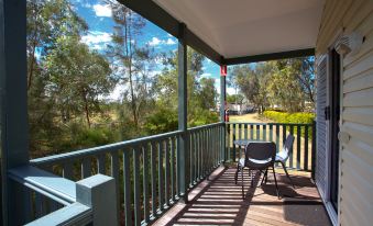a wooden deck with a railing and outdoor furniture , overlooking a lush green field and trees at Discovery Parks – Biloela