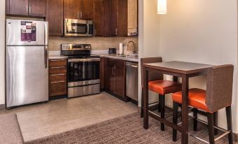 a kitchen with wooden cabinets , a refrigerator , and a microwave oven is shown next to an island with stools at Residence Inn St. Louis Westport
