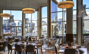 a large , modern restaurant with wooden floors and high ceilings , surrounded by windows offering a view of the city at Novotel Sydney Darling Harbour