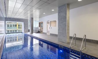 an indoor swimming pool with blue tiles , surrounded by white walls and a staircase leading to the water at IStay Precinct Adelaide
