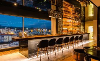 a modern bar with black chairs and a wooden counter , overlooking a cityscape at dusk at Octant Ponta Delgada