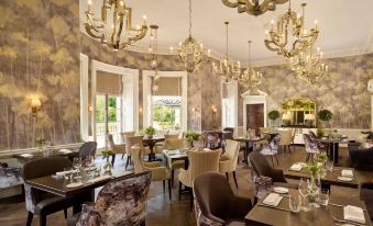 a luxurious restaurant with multiple dining tables and chairs , chandeliers hanging from the ceiling , and a pool in the background at The Langley, a Luxury Collection Hotel, Buckinghamshire