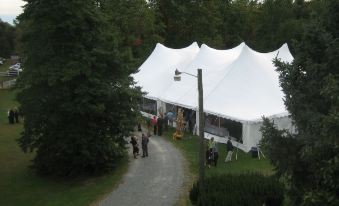 a group of people gathered in a wooded area , walking down a path towards a large white tent at Inn at Mitchell House