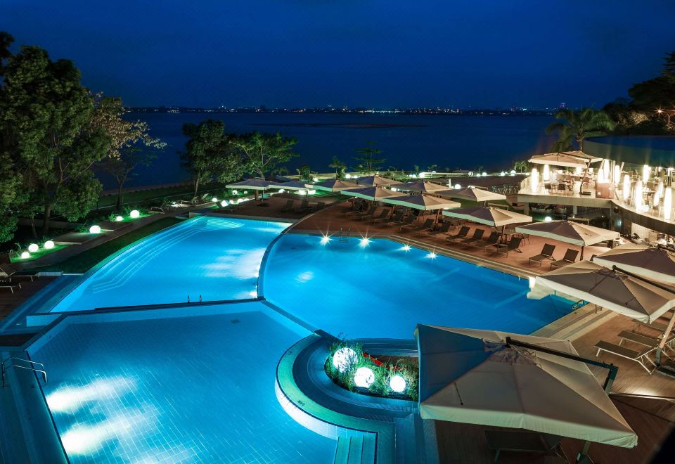 a large outdoor swimming pool surrounded by grass , with several lounge chairs and umbrellas placed around the pool area at Radisson Blu M'Bamou Palace Hotel, Brazzaville