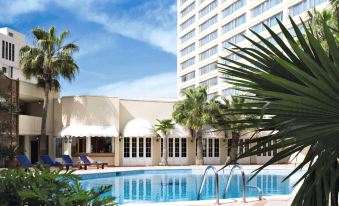a large swimming pool is surrounded by palm trees and a tall building with white columns at Amman Marriott Hotel