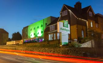 "a large building with a green and white sign that says "" holiday inn "" is illuminated at night" at Holiday Inn Sittingbourne
