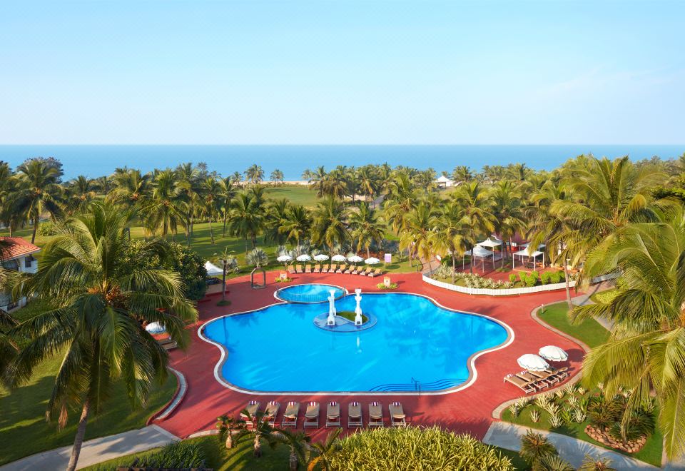 a large , red - roofed resort with a swimming pool surrounded by palm trees and lush greenery at Holiday Inn Resort Goa