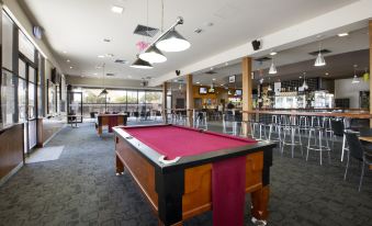 a pool table with a red cloth is in the middle of a room with bar stools and pendant lights at Nightcap at Playford Tavern