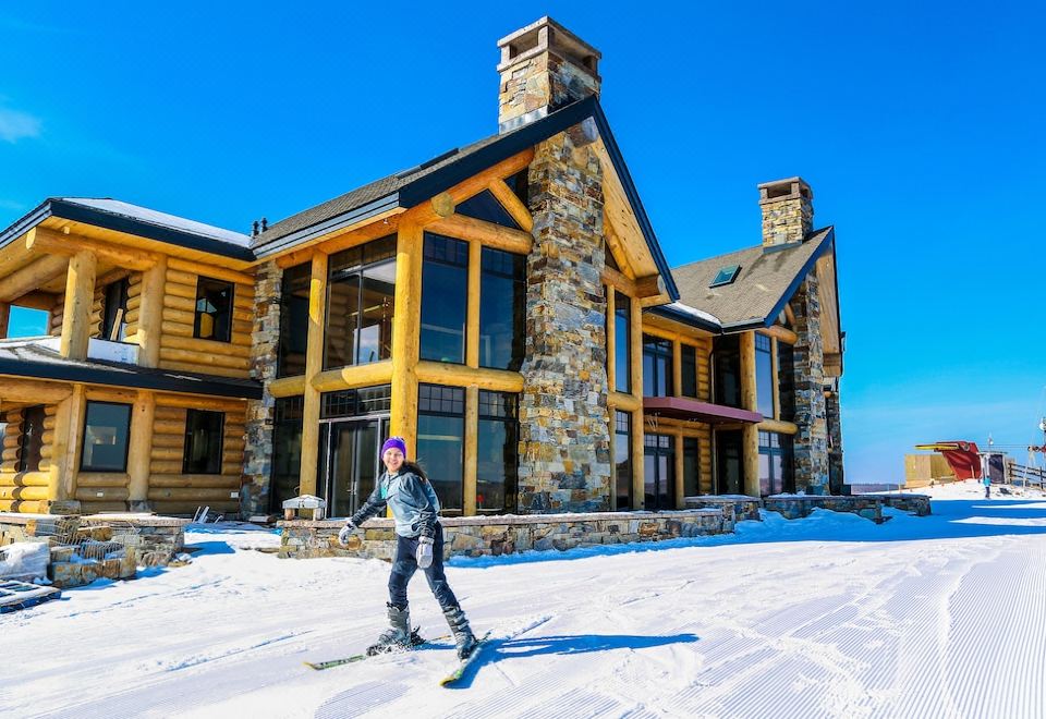 a man is skiing down a snow - covered slope next to a large house , enjoying the winter scenery at Mont du Lac Resort