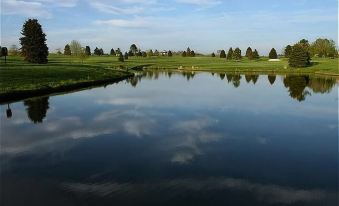 a serene landscape of a lake with trees and clouds reflected in the water , under a clear blue sky at Ramada by Wyndham Clarion
