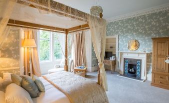 a luxurious bedroom with a four - poster bed , a fireplace , and a large window overlooking a lush green landscape at Balcary House Hotel