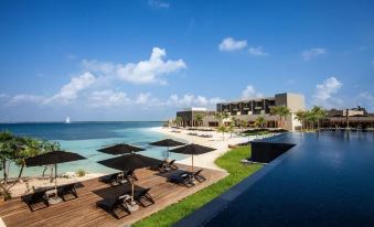 a beachfront resort with a pool , umbrellas , and lounge chairs , surrounded by palm trees and the ocean at Nizuc Resort & Spa