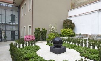 a modern building with a large black sculpture in the courtyard , surrounded by greenery and flowers at Hotel Maribor & Garden Rooms