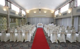 a large , empty banquet hall with white chairs and a red carpet leading to a long banquet table at Best Western Heronston Hotel  Spa