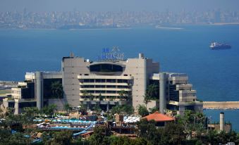 a large hotel surrounded by trees and water , with a view of the ocean in the background at Le Royal Hotel - Beirut