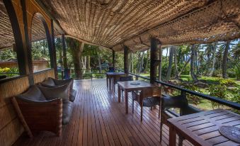 a wooden deck with several tables and chairs , providing a comfortable outdoor dining area surrounded by lush greenery at Maravu Taveuni Lodge