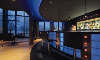 a modern bar with black chairs and tables , a curved counter , and large windows that offer views of the outside at Radisson Hotel Zurich Airport