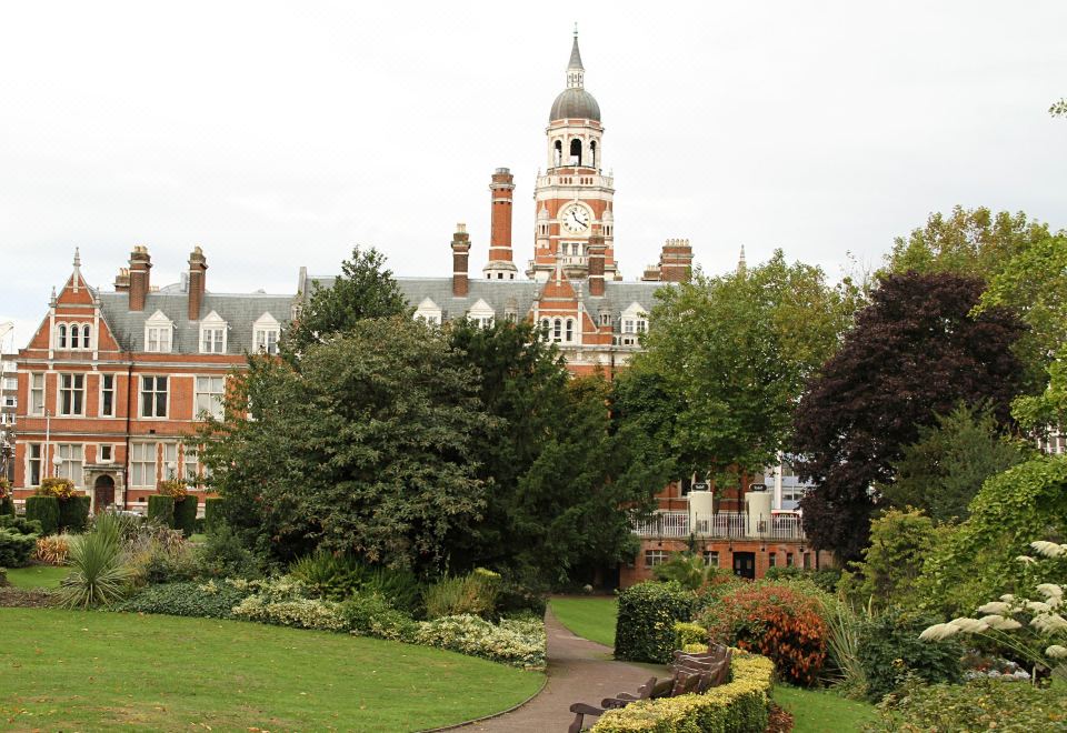 a large red brick building with a clock tower , surrounded by lush green trees and a walkway leading to it at Lansdowne Hotel