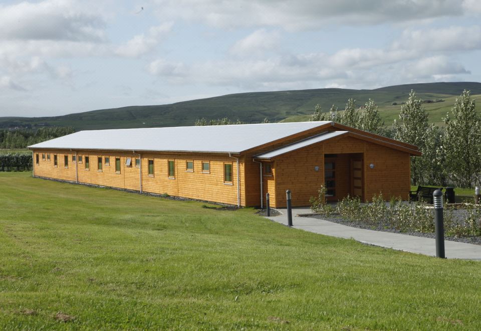 a wooden building with a white roof is surrounded by a green field and hills at Hótel Eyjafjallajökull