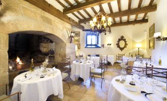 a dining room with a fireplace in the background and several tables covered in white tablecloths at Parador de Cangas de Onis