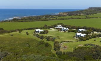 aerial view of a large , well - maintained green field with several white houses and a view of the ocean in the background at Bear Gully Coastal Cottages