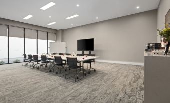 a conference room with a large table surrounded by chairs and a television mounted on the wall at Quest Innaloo