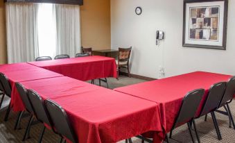 a conference room with several tables covered in red tablecloths , chairs , and a window in the background at Comfort Suites