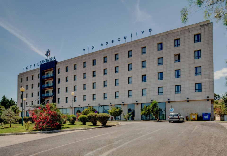 a large hotel building with a parking lot in front of it , surrounded by trees at VIP Executive Santa Iria Hotel