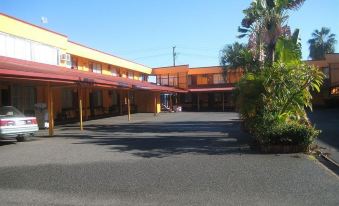 a large building with a parking lot in front of it , surrounded by trees and bushes at Ambassador Motel