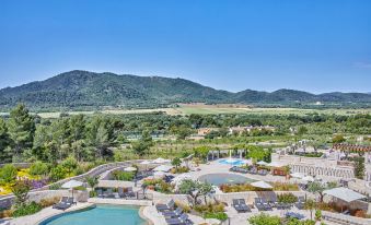 a beautiful resort with a swimming pool surrounded by lush greenery , mountains in the background , and clear blue skies at Cap Vermell Grand Hotel