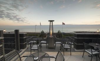 a rooftop patio with a fire pit and tables , overlooking the ocean at sunset , under an overcast sky at Cbh Hythe Imperial Hotel Golf and Spa