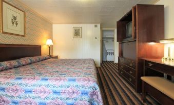a hotel room with a bed , dresser , and dresser chair , along with the door leading to another room at Colony Motel Jamestown