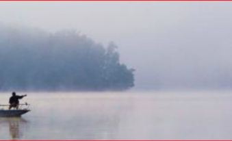 a foggy lake with a small island in the middle , surrounded by trees and a cloudy sky at Lamplight Inn