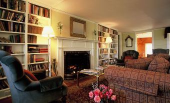 a cozy living room with a fireplace , bookshelves filled with books , and a fireplace in the background at Dexter's Inn