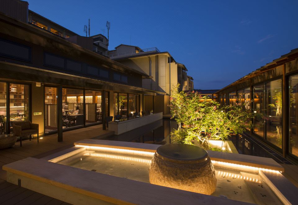 a courtyard with a fountain in the center , surrounded by buildings and lit up at night at Biwako Ryokusuitei