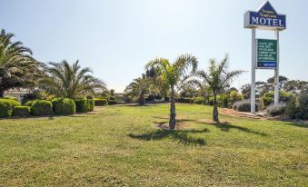 a grassy field with palm trees and a blue sign for the motel on the side at Torquay Tropicana Motel