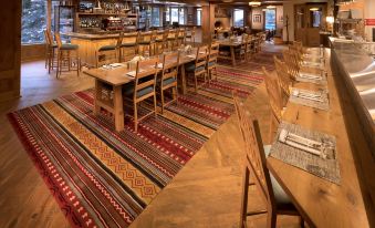 a large dining room with wooden tables and chairs , surrounded by a bar area with stools at The Blake at Taos Ski Valley