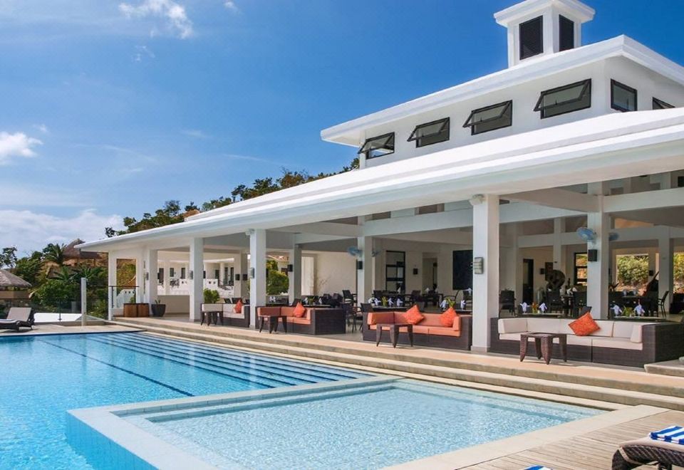 a large white building with a swimming pool in front of it , surrounded by chairs and tables at Busuanga Bay Lodge