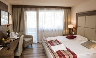 a hotel room with a large bed , a chair , and a window overlooking the city at Hotel Ambassador Zermatt