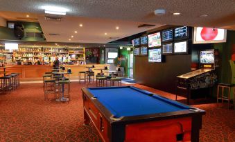 a pool table in a bar area , surrounded by chairs and tables , with multiple televisions mounted on the wall at Prince of Wales Hotel