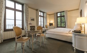 a luxurious hotel room with a large bed , white curtains , and a balcony , as well as a dining area with chairs at Grandhotel Giessbach